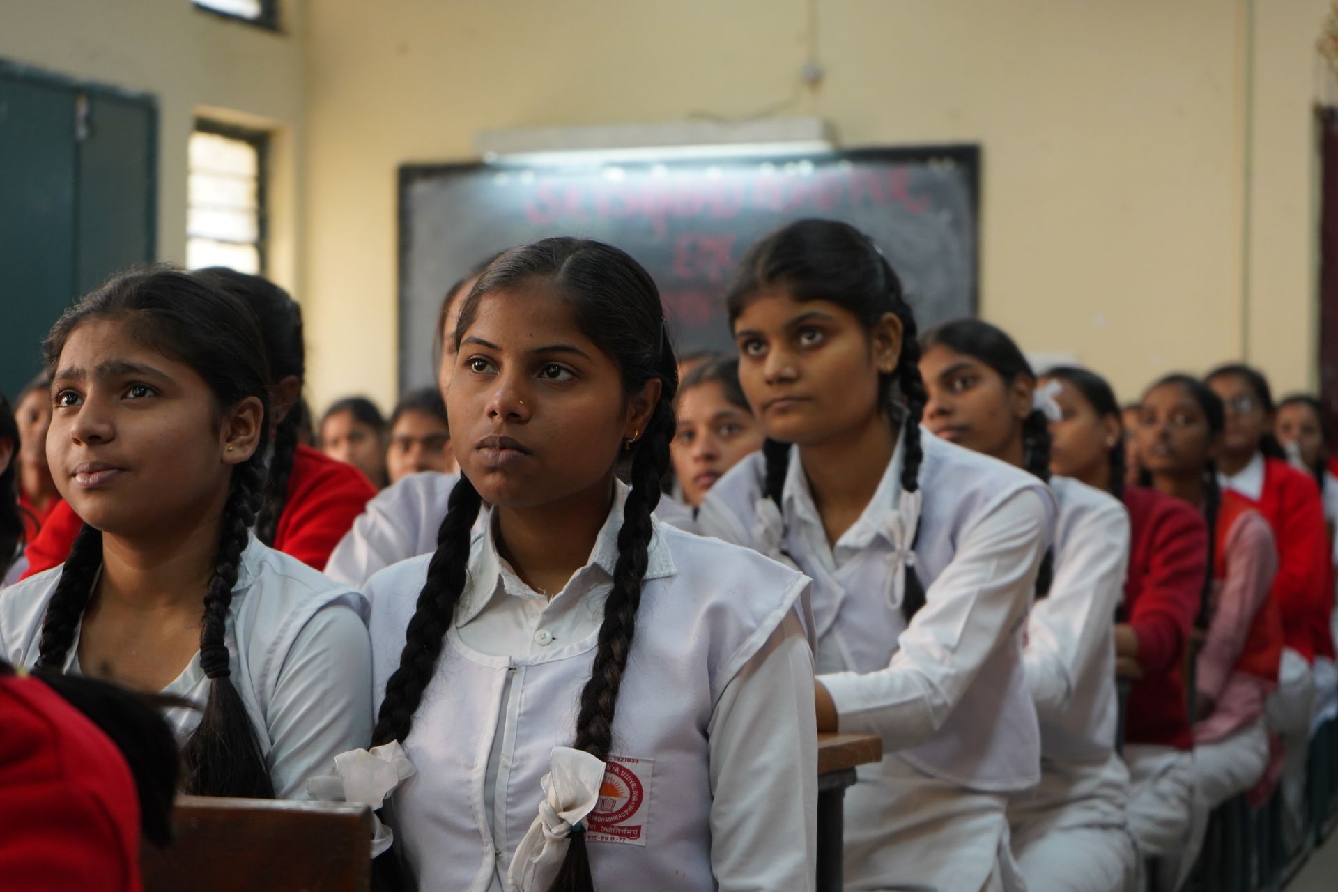 Indian schoolgirls in white uniforms with braided hair listening attentively in a classroom