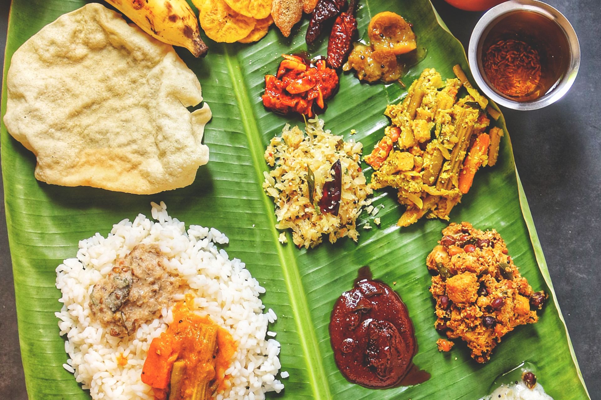Overhead view of a sadya with rice, curries, pickles, papadam and banana on a banana leaf