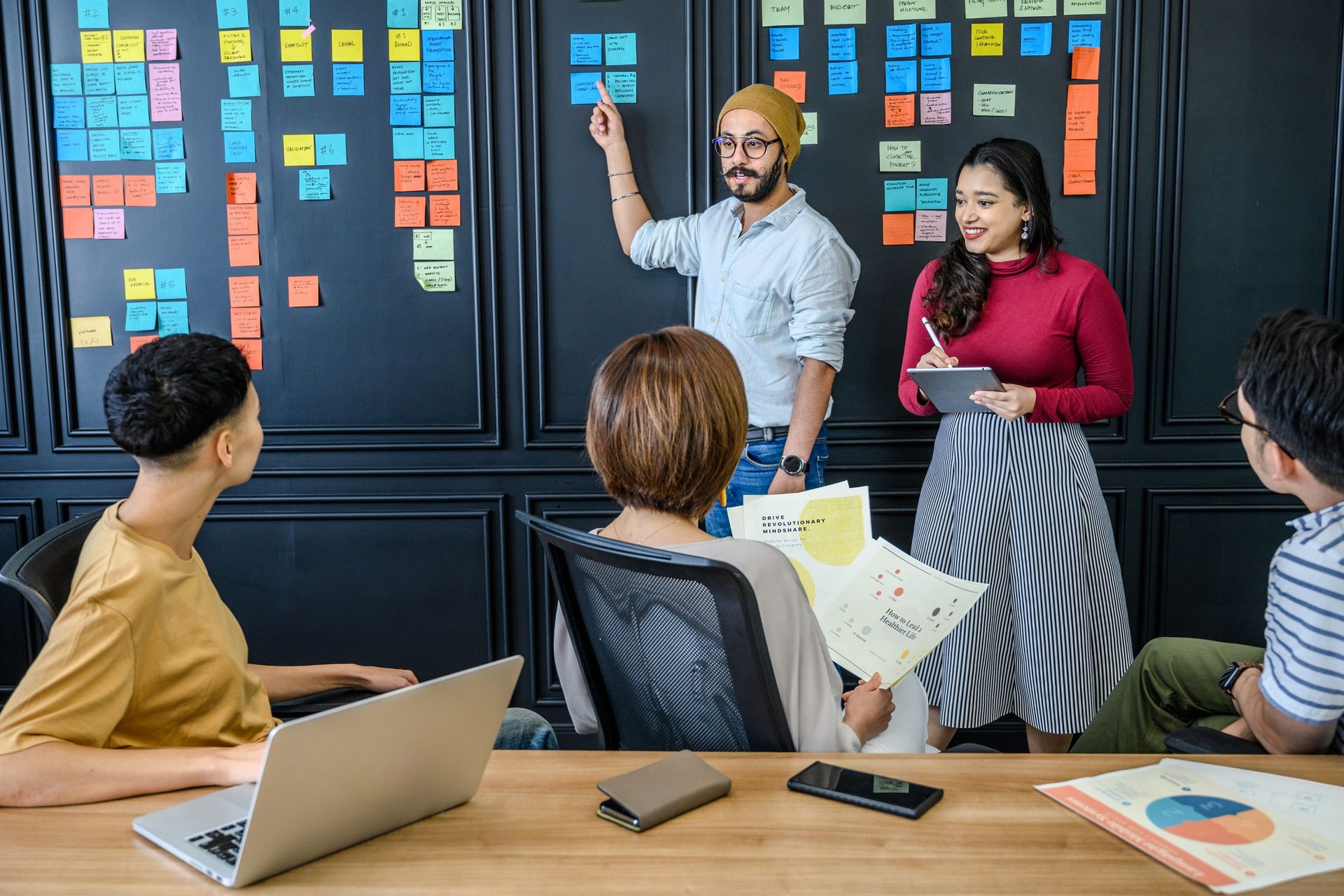 Man points at a wall of sticky notes while a team reviews the plan