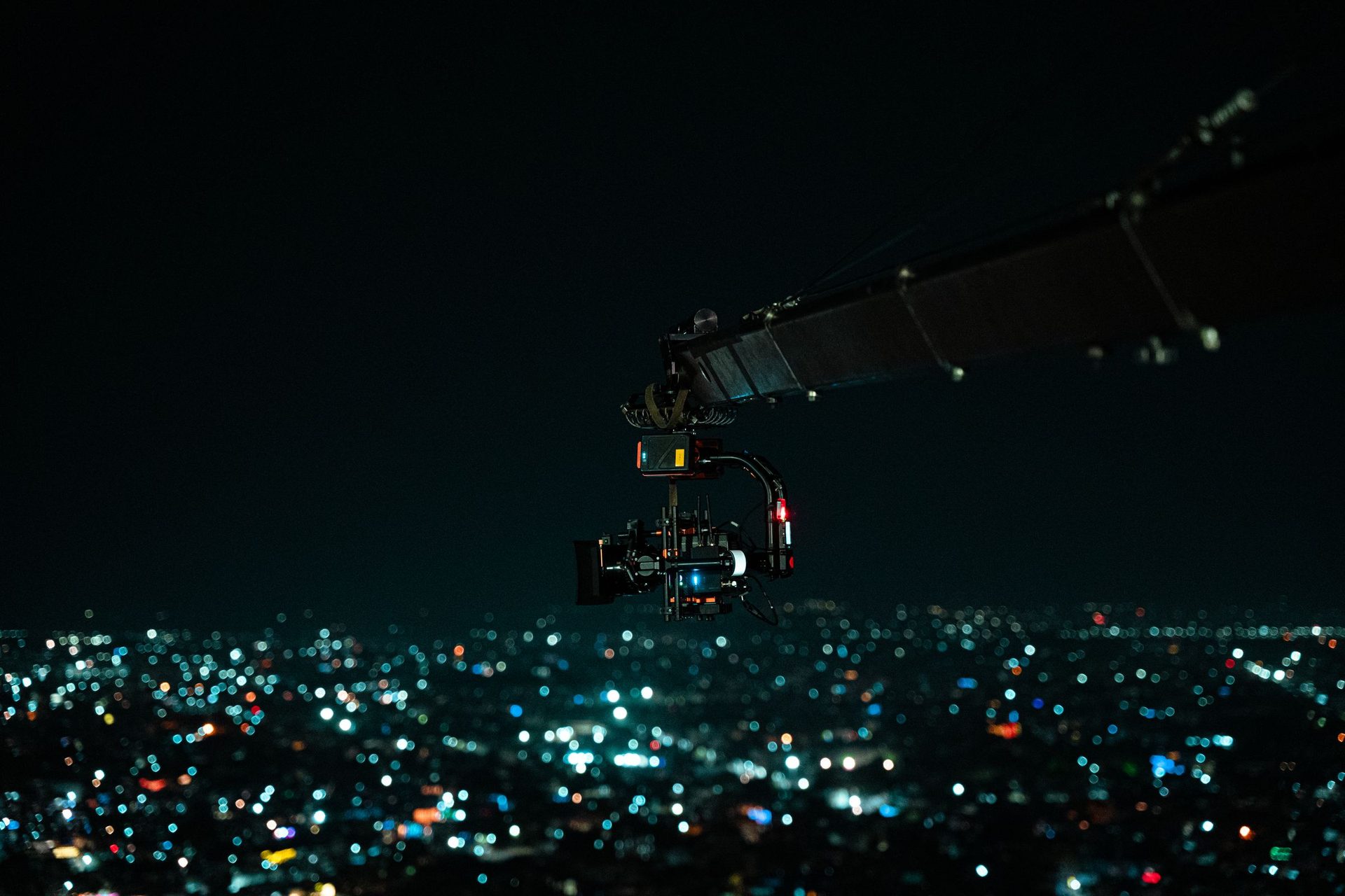 Camera on a gimbal at the end of a crane arm above city lights at night